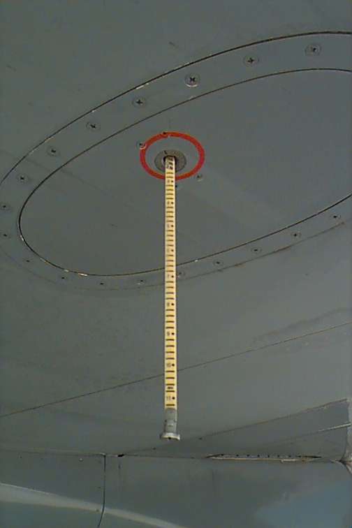 A fuel dripstick extended from the underside of a commercial aircraft wing, showing the graduated measuring scale used to manually verify fuel quantity